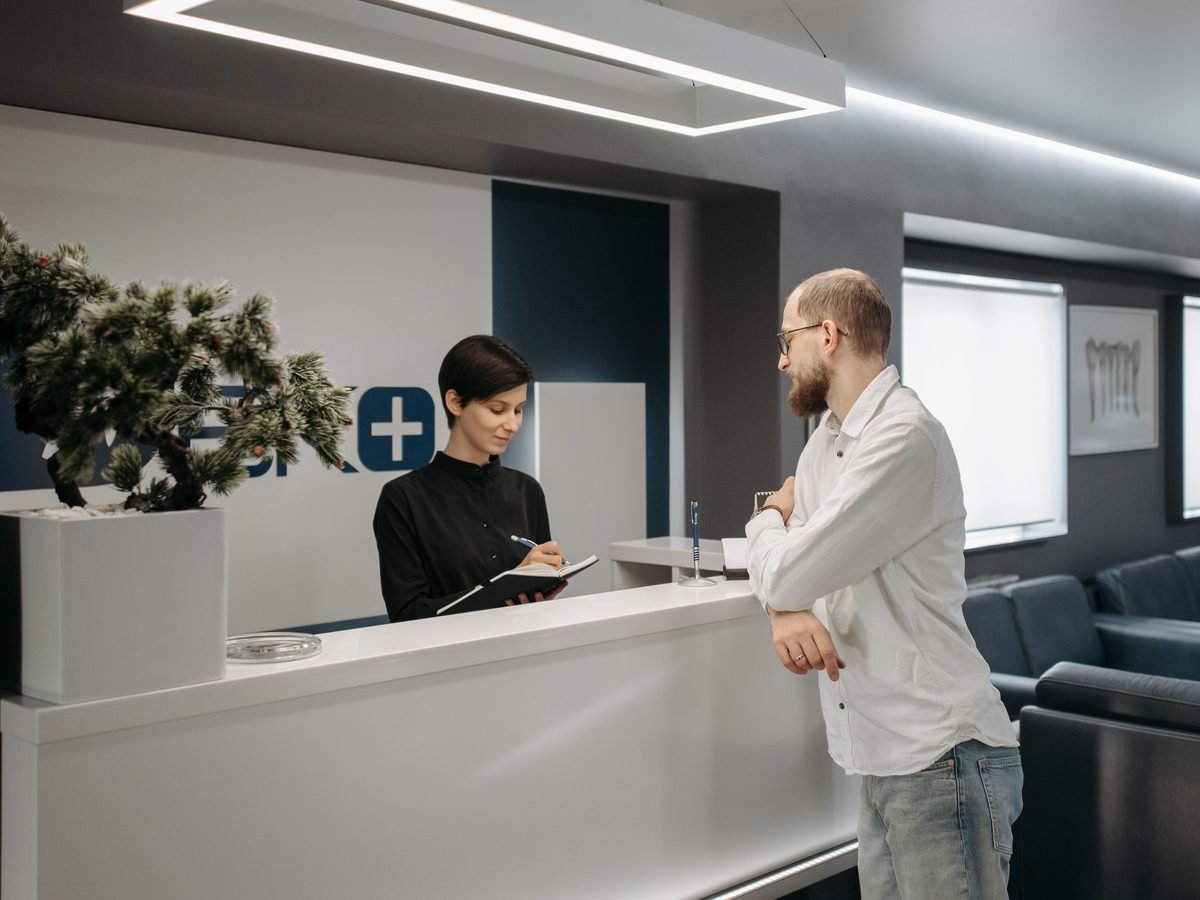 A patient speaking to staff at a clinic reception desk